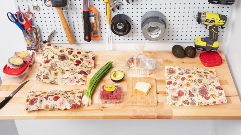 A workstation with Bee's Wrap produce bags, scallions, avocado, and a slice of bread.