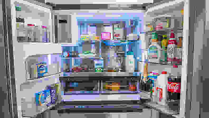 A shot of the interior of the Midea MRQ22D7AST French-door fridge, fully stocked with groceries. Its interior is illuminated by an LED array, which is casting a cool-colored light on the front and sides of everything inside. Each item is very easy to see.