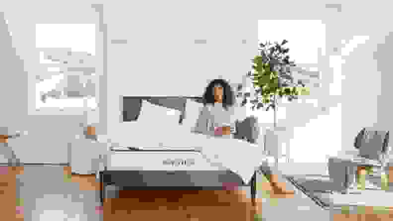 a person sits on the awara mattress in a white room with a brown, wood floor