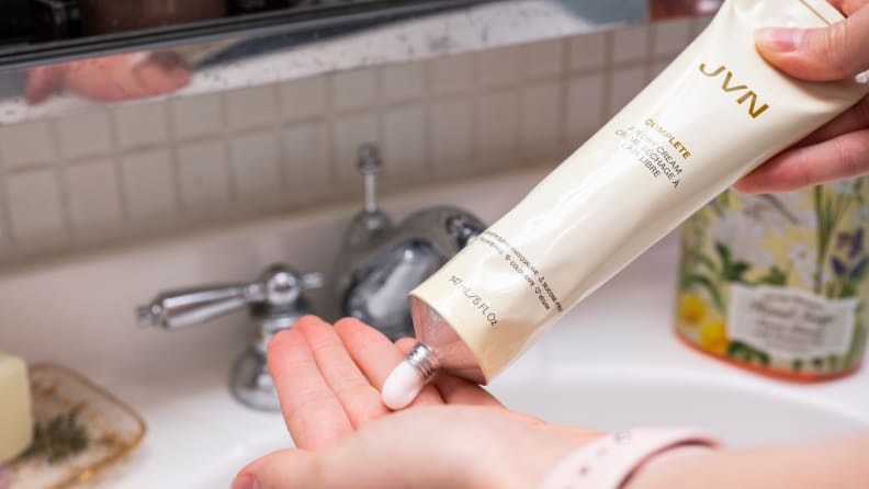 A hand squeezing a tube of hair cream into the other hand.