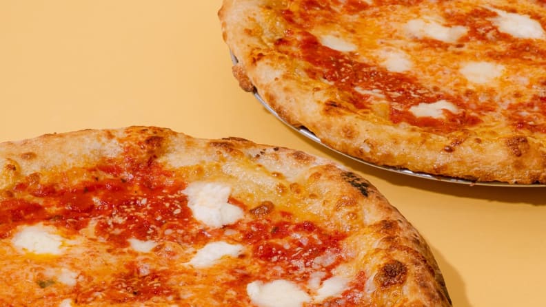Two cheese pizzas on a yellow surface.