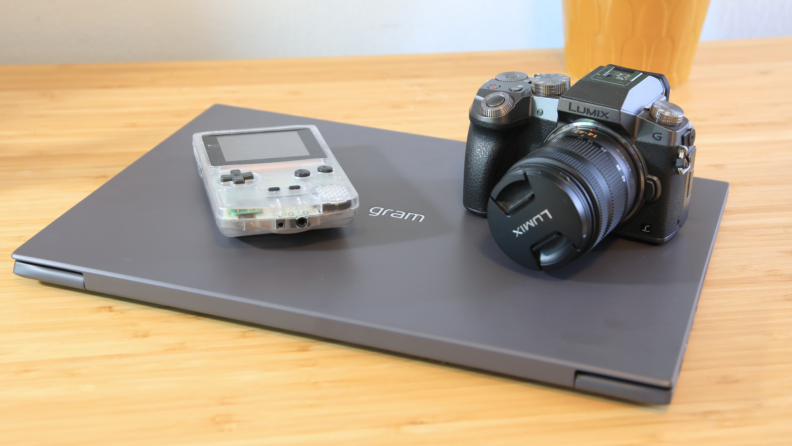 A Gameboy and a camera sit on top of a laptop computer.