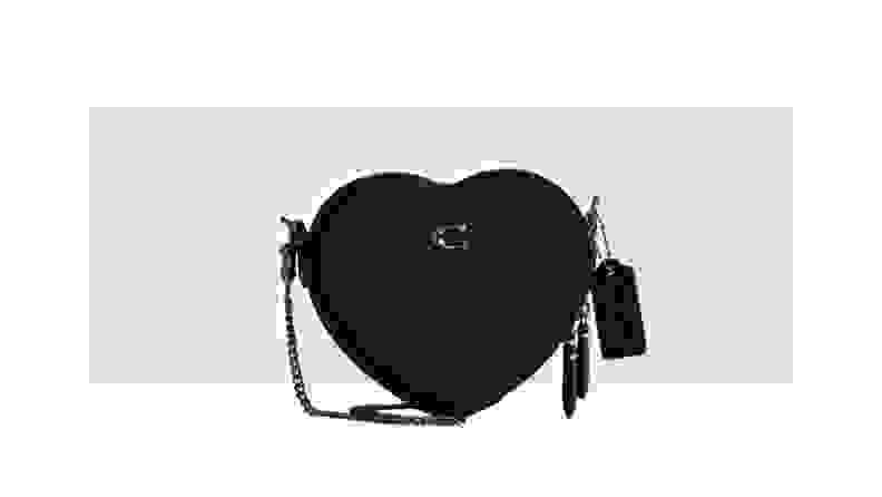 A black leather crossbody bag in the shape of a heart.