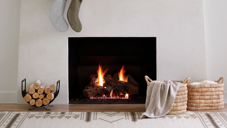 A mantle with a fireplace, firewood, woven boxes with a throw, a rug, and two linen stockings