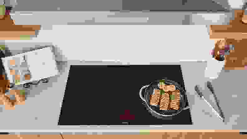 A top-down photo of an induction cooktop with a pan filled with fish cooking on top.