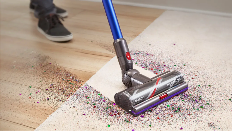 A Dyson cordless vacuum, vacuuming up dirt on a rug.