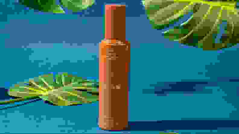 A tan bottle of face lotion against a blue background and foliage.