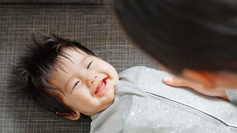 Smiling Asian baby in grey swaddle.