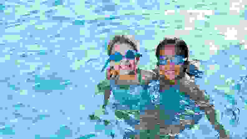 Two girls hug each other and smile in a pool.