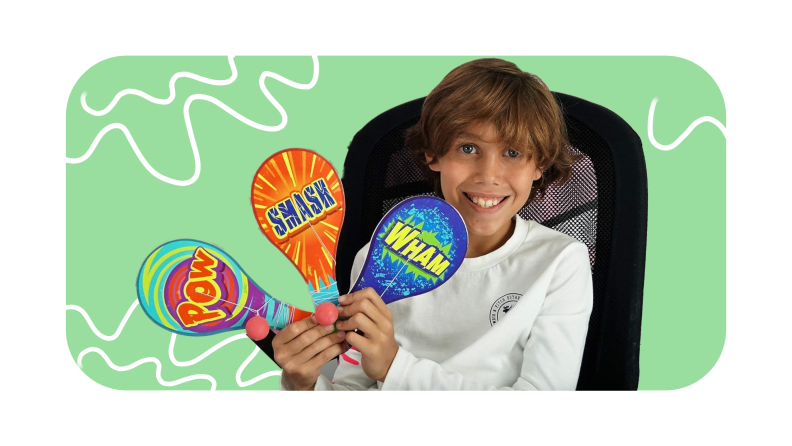 Child holding up three paddle toys with ball attached by string while sitting in office chair.