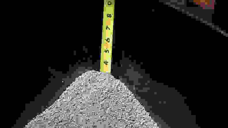 A tape measure is used to determine the depth of cat litter inside of a litter box.