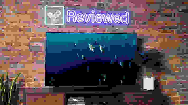 An image of penguins swimming on the LG C2 OLED sitting on a wooden table in front of a brick wall with a Reviewed neon sign hanging behind it.