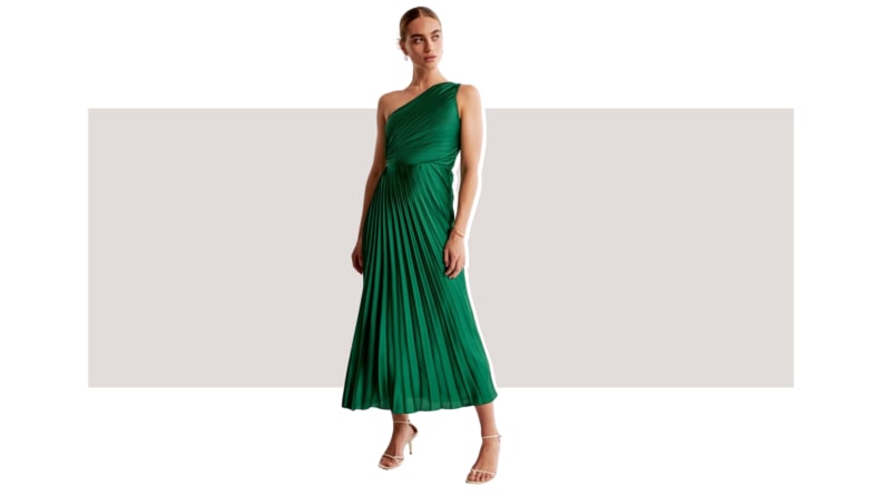 A model wearing a pleated emerald green dress that has a one-shoulder design.