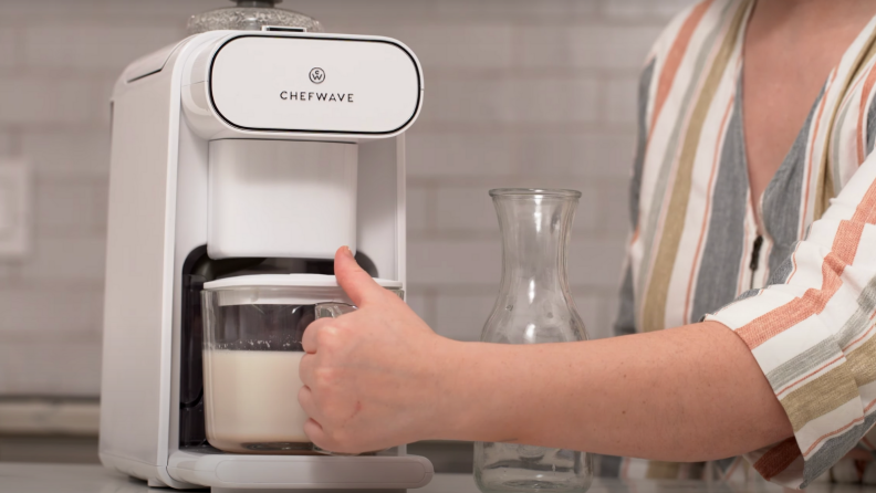 A person is removing the pitcher from the ChefWave vegan milk maker.
