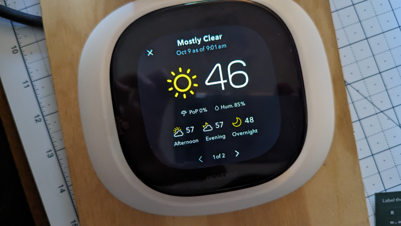 A white smart thermostat reads 46 degrees and sunny weather