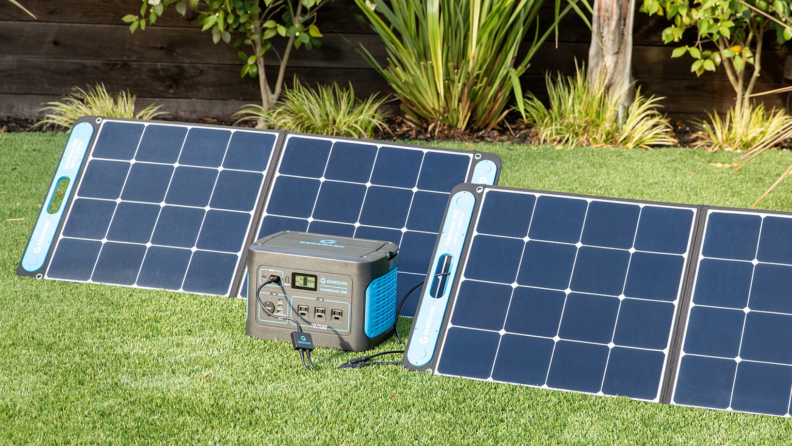 Solar panels charging outdoors on grass next to portable generator.
