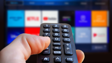 Person holding remote in front of smart TV with different streaming widgets on screen.