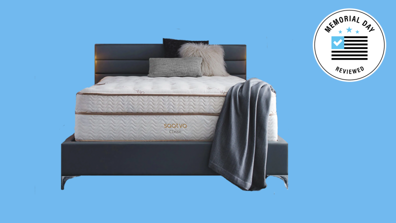 A Saatva mattress on a bedframe against a blue background.