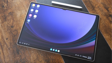 Samsung Galaxy Tab S9 Ultra tablet with desktop display on LED screen next to white S stylus pen on top of wooden surface.