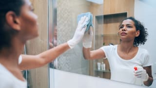 女士戴上清洁手套，用喷瓶和抹布擦拭镜子。