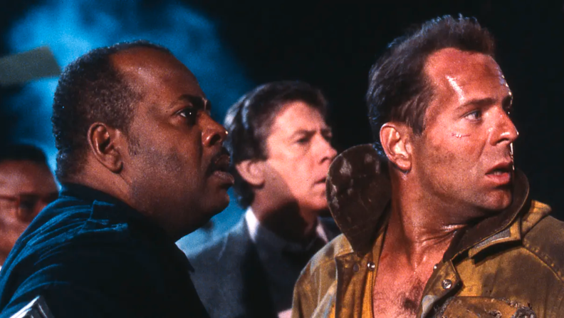 In Die Hard (1988), a befuddled and victorious dynamic duo of John McClane and Al Powell (Bruce Willis and Reginald VelJohnson, respectively) look back at a burning tower after taking down notorious baddy Hans Gruber, played by the late Alan Rickman.