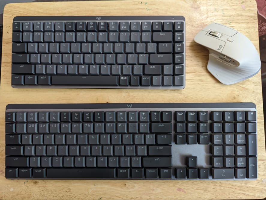 Two different sized keyboards next to a computer mouse on top of a table