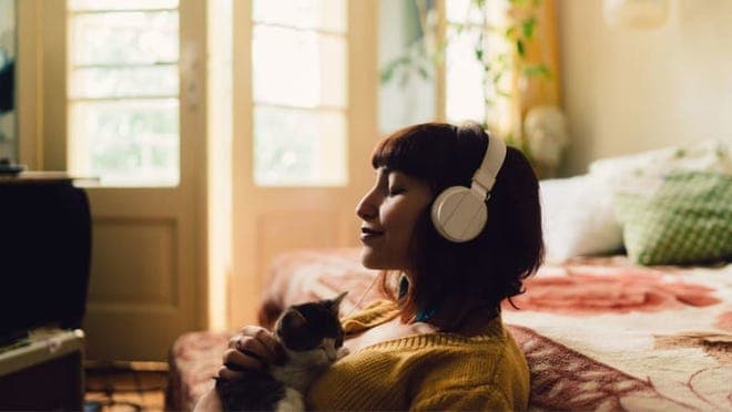 A person wearing headphones holds a kitten.