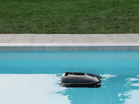 A black, square robot floats on the surface of a swimming pool
