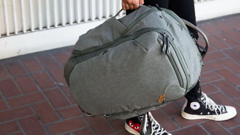 A model holds a Peak Design Travel Backpack 45L by one of its handles.