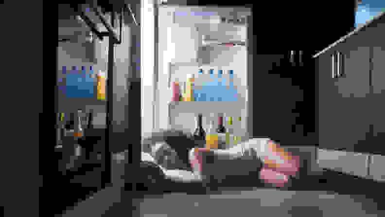 A woman has fallen asleep in front of her open refrigerator door.