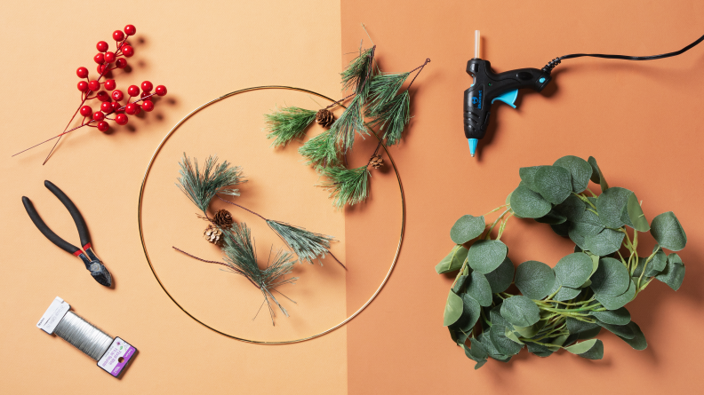 A table filled with a brass ring, fake flowers, wire, and a hot glue gun.