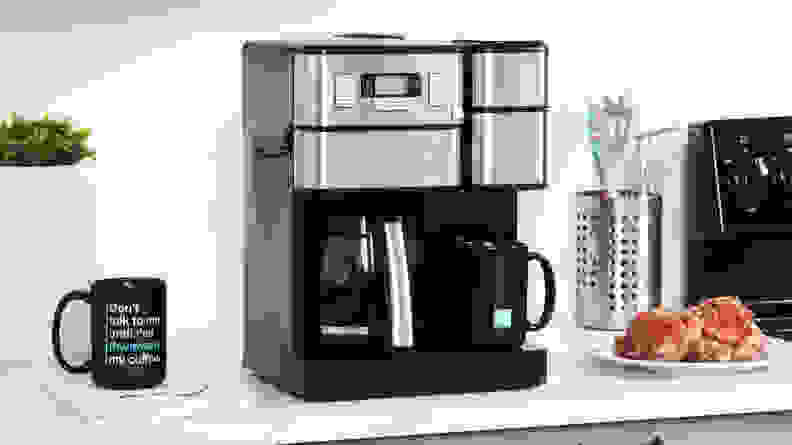 The silver and black Cuisinart coffee machine on a counter next to a coffee mug and plate of pastries.