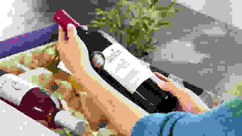A woman holding a bottle of wine above a Firstleaf package.