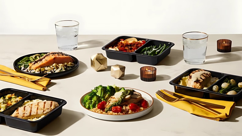 Tabletop display of Factor meals in black containers and plated servings, featuring salmon, chicken, vegetables, and pasta.