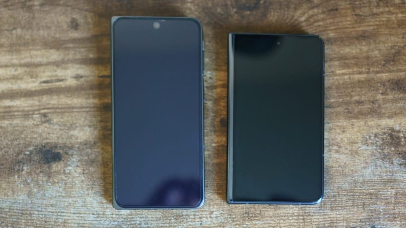 The OnePlus Open and the Google Pixel Fold smartphones face up, side by side on top of a wooden surface.