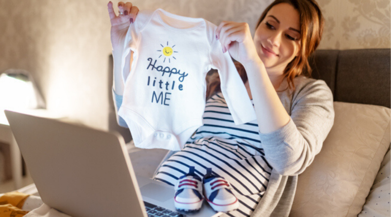 Woman holds up baby onesie to computer screne
