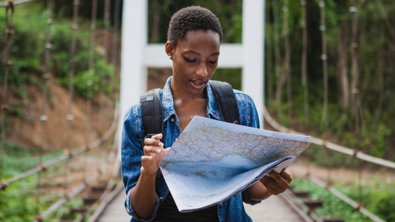 A person walks across a bridge while looking at a trail map.