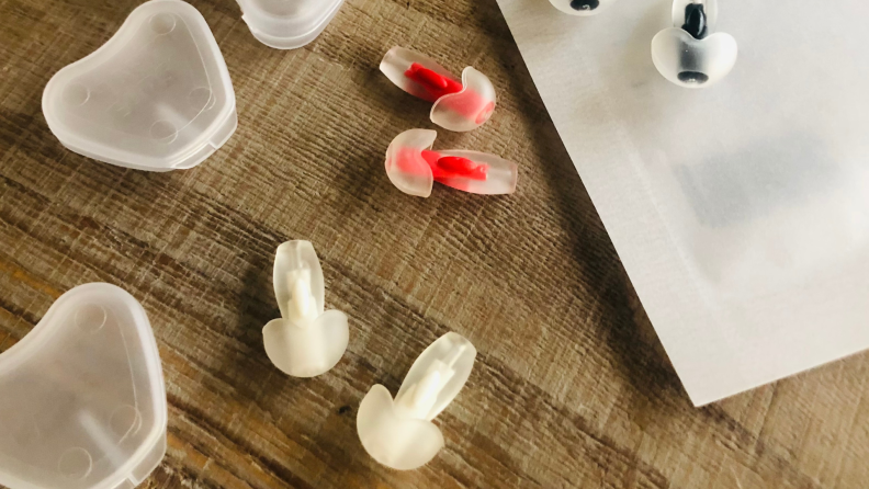 Happy Ears Earplugs next to original packaging and three carrying travel cases on top of wooden table surface.