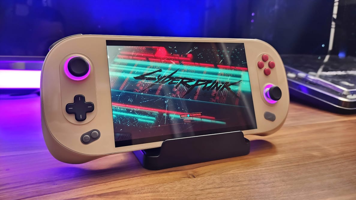 Ayaneo 2S Handheld gaming computer on top of stand on hardwood surface in front of colored LED light strip.