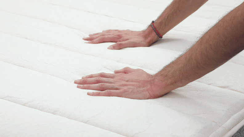 Two hands pressing down on the Birch Natural Mattress, presumably kicking up the new product smell.