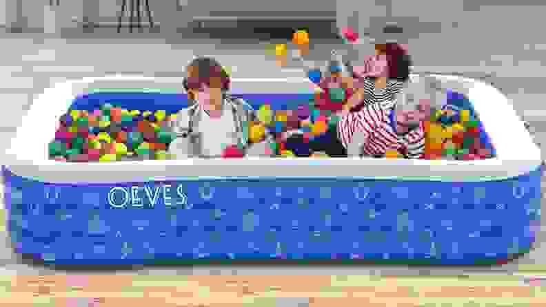 Four children play in an inflatable pool filled with plastic balls.