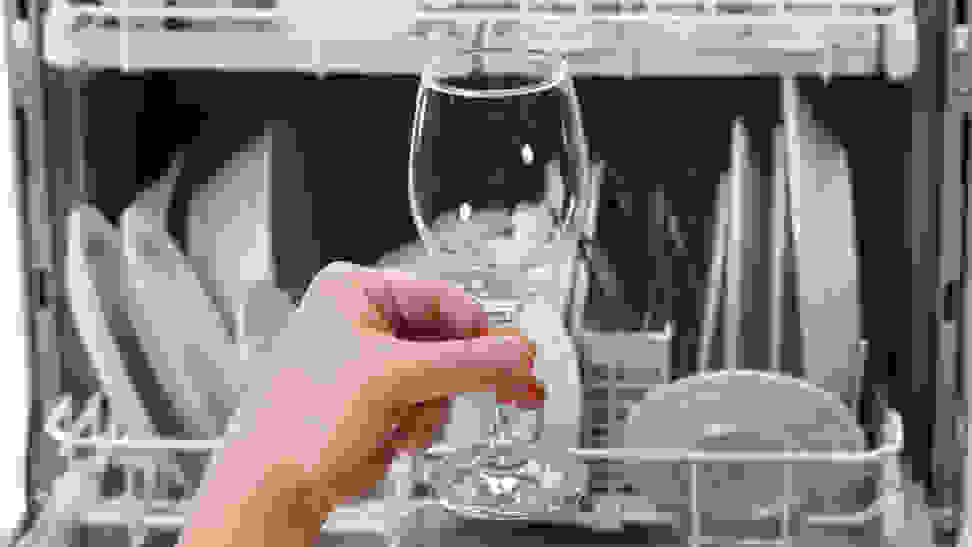 Someone examines a wine glass upon taking it out of the dishwasher.