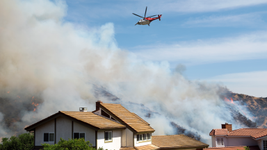 Plane flies above residential homes covered in smoke during wildfire.