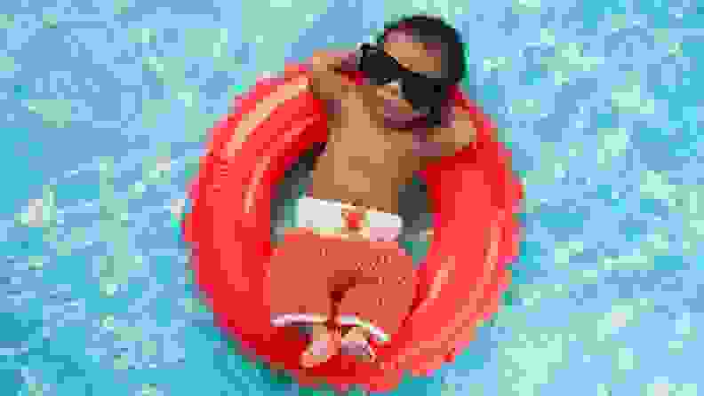 A newborn baby boy sleeping on a tiny inflatable swim ring. He is wearing crocheted board shorts and black sunglasses.
