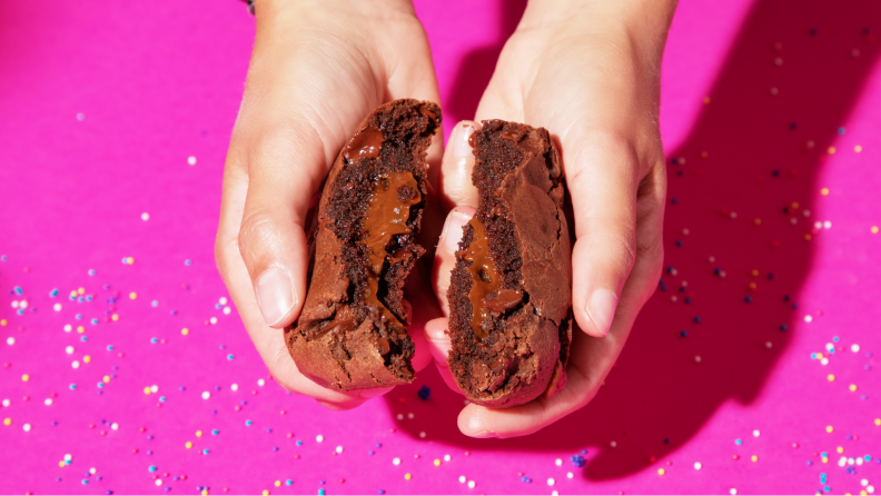 A pair of hands splitting the chocolate-stuffed chocolate fudge cookie.