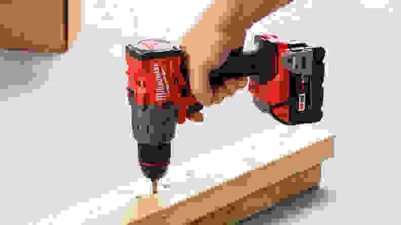 A person using the Milwaukee M18 Cordless Hammer Drill to drill a nail into a slim wood panel.