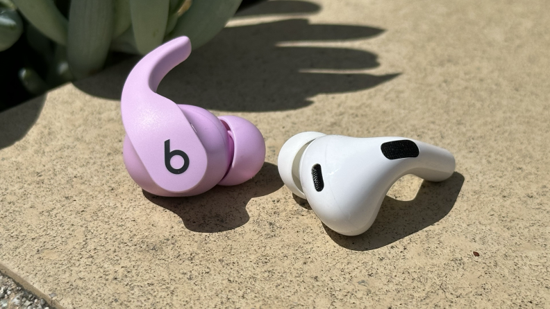 A purple Beats Fit Pro earbud next to an AirPods Pro 2 earbuds sitting on a wall.