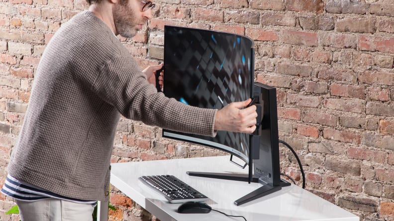 A person holding the Corsair Xeneon Flex monitor, that's sitting on a white table with a brick background.