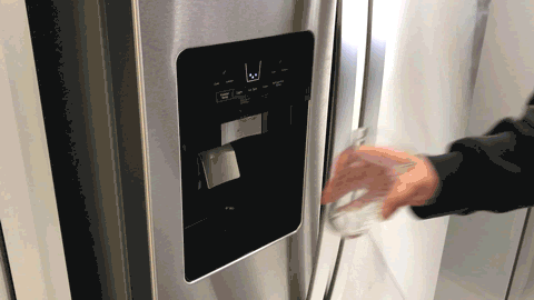 Person using water dispenser on the Whirlpool WRS331SDHM to fill glass.