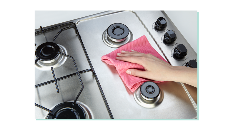 Person using pink rag to polish and clean in between grates on stove top.